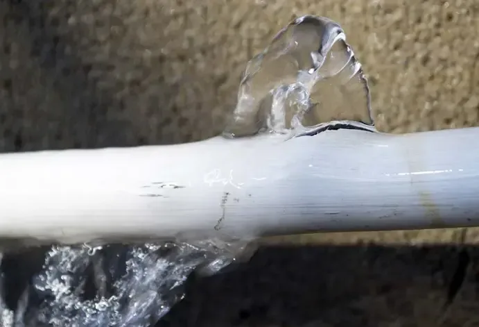Water spraying from a split opening in a white pipe