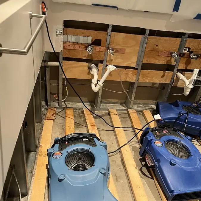 Air movers sit beneath exposed sink plumbing where cabinetry has been removed