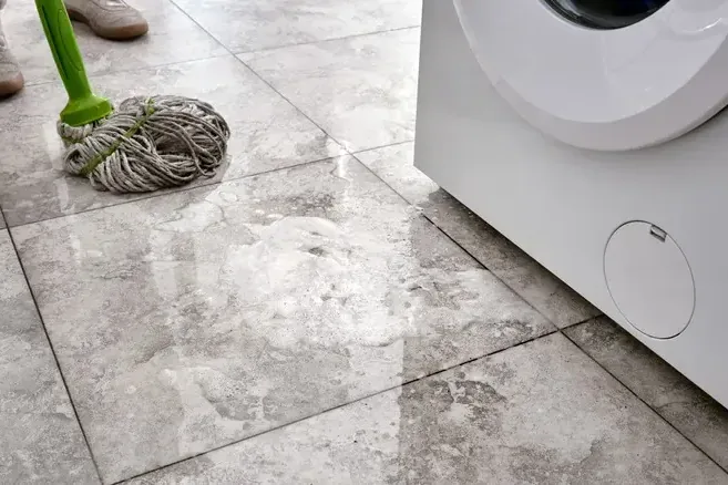 A mop rests on wet tile beside a white washing machine