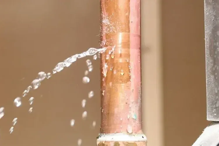 Water sprays from a damaged copper supply pipe mounted beside a wall