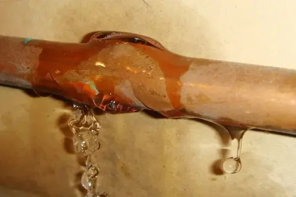 Water drips from a wide split in a copper supply pipe